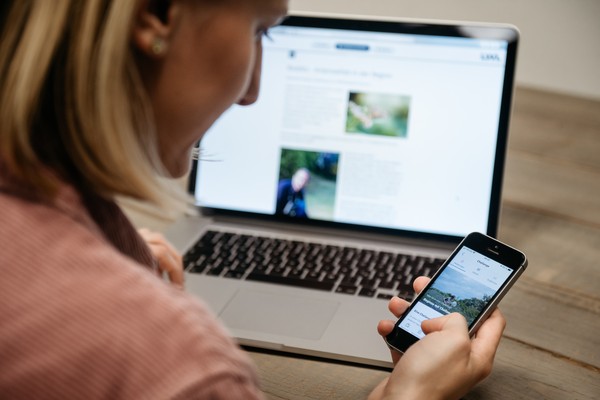 Eine Frau sitzt vor einem PC mit einem Handy in der Hand. Foto: LWL/Steinweg