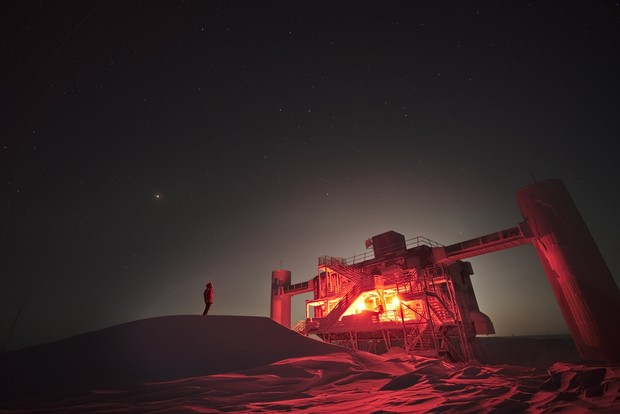 Ein Mensch steht bei Nacht vor einer Forschungsstation in der Eiswüste des Südpols.