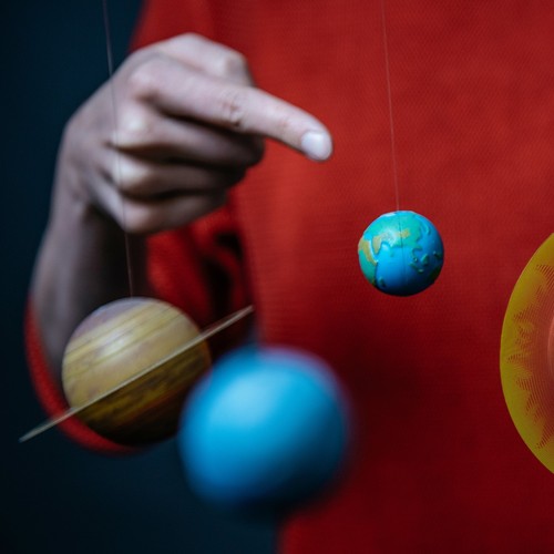 Der Finger einer Person zeigt auf kleine Planeten-Modelle.