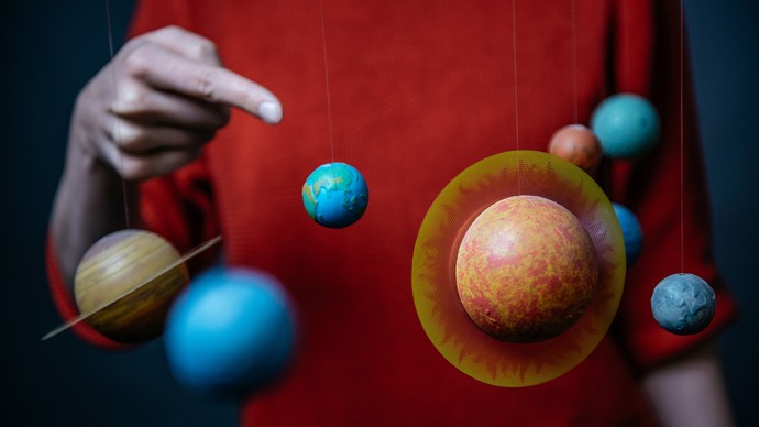 Der Finger einer Person zeigt auf kleine Planeten-Modelle. Der Finger einer Person zeigt auf kleine Planeten-Modelle.