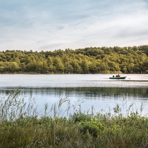 Ein See mit einem kleine Boot darauf und grünen Bäumen im Hintergrund.