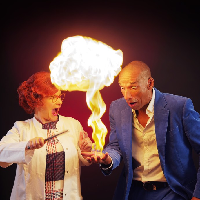 Eine Frau hält Feuer in der Hand ein Mann schaut erstaunt auf die hohe Stichflamme. (vergrößerte Bildansicht wird geöffnet)