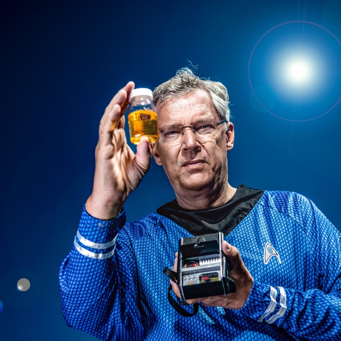 Ein Mann in Starfleet-Uniform mit Transponder in der einen Hand und einem kleinen Döschen in der anderen Hand. (vergrößerte Bildansicht wird geöffnet)