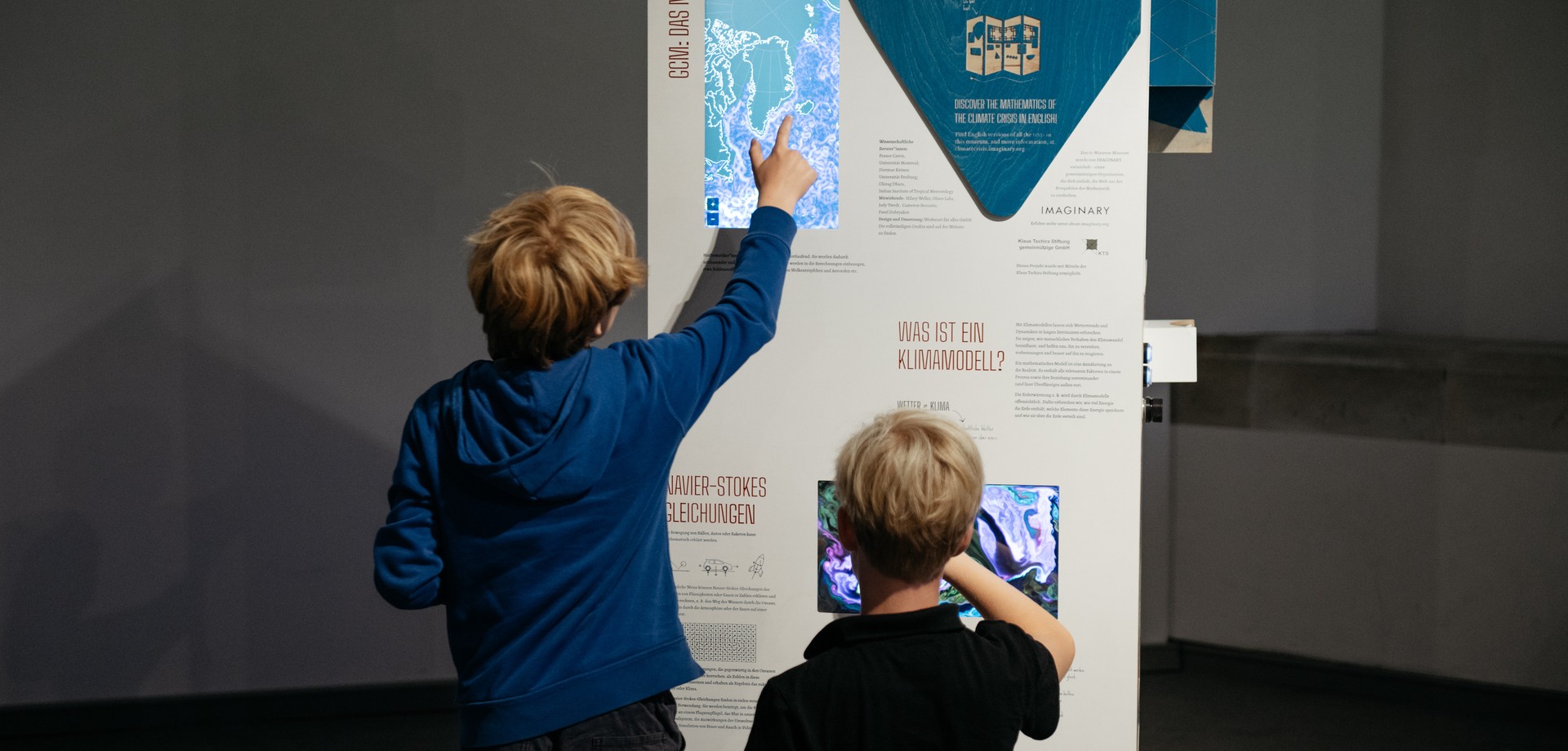 Kinder stehen vor einer Stele mit Ausstellungsinformationen und Bildern.