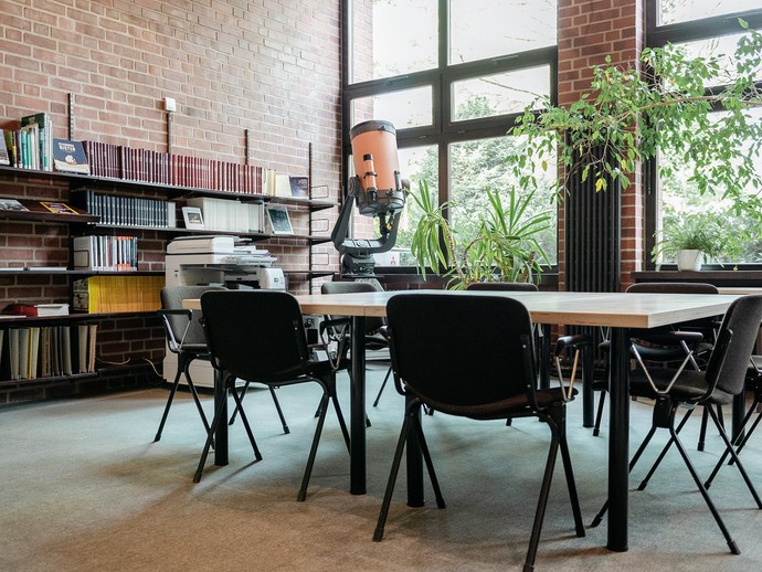 Offene Bücherregale, davor mehrere Tische und Stühle vor großen Fenstern. (vergrößerte Bildansicht wird geöffnet)