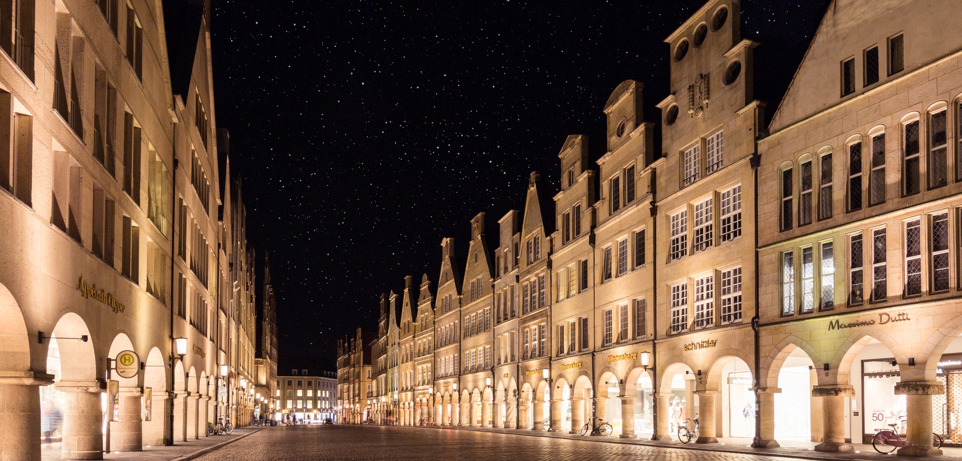 Der Münsteraner Prinzipalmarkt mit beleuchteten Giebelhäusern bei Nacht und dem Sternhimmel darüber.