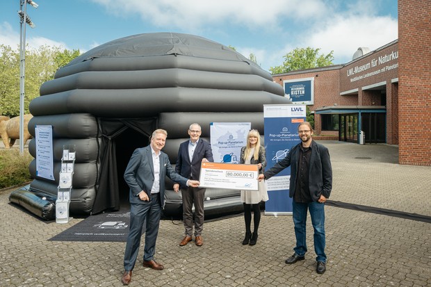 Vertreter der Stiftung Sparkasse Münsterland Ost überreichen einen Scheck an Vertreter des LWL vor dem Pop-up-Planetarium.