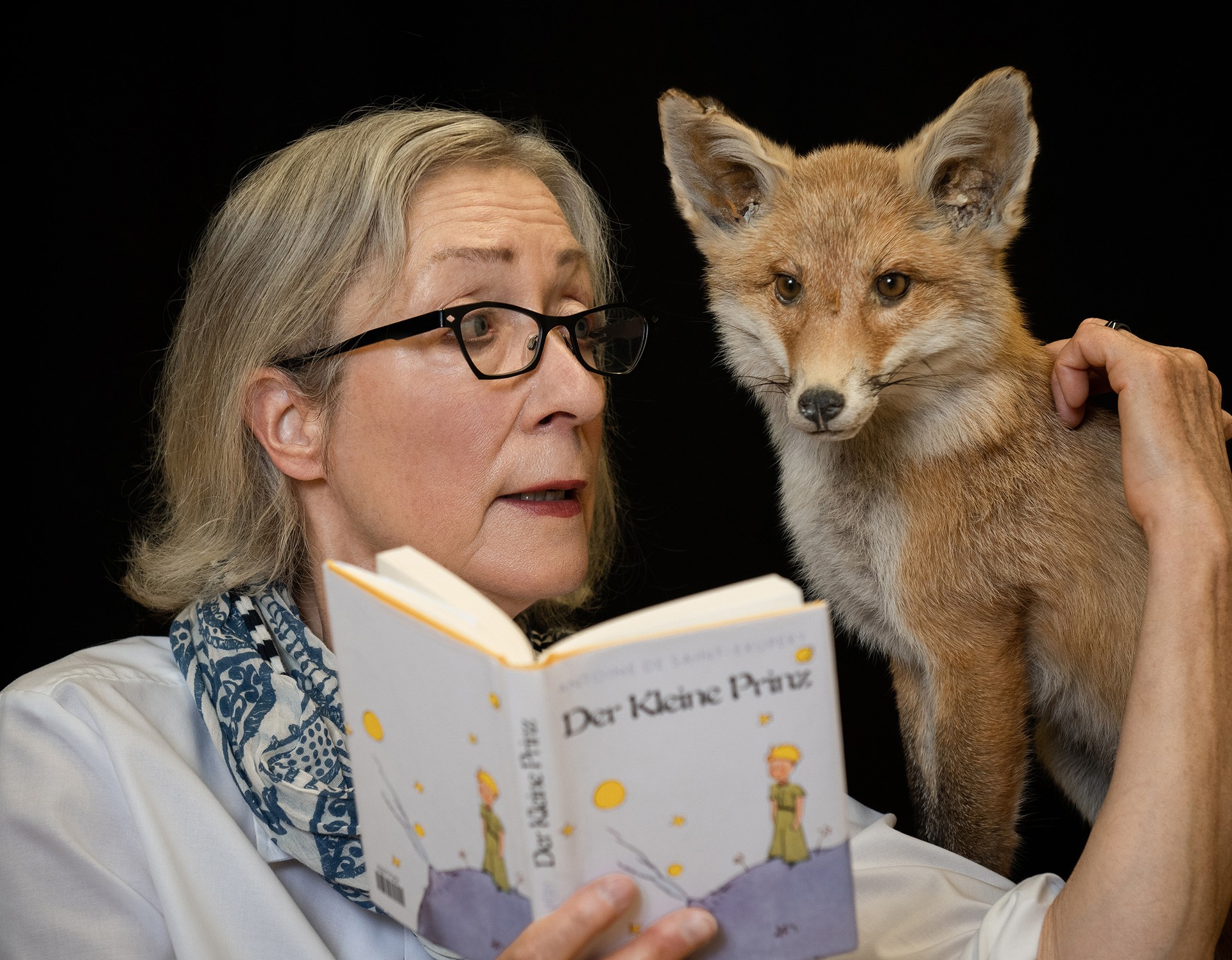 Frau mit einem präparierten Fuchs liest aus einem Buch.