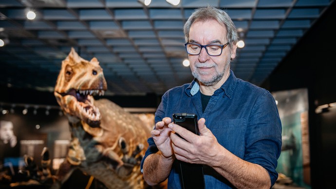 Visitor stands in front of a dinosaur with a mobile phone.