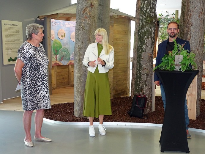 Die Bürgermeisterin von Bünde, LWL-Kulturdezernenting und der Museumsdirektor aus Münster stehen vor Bäumen nd Holzhütte an Stehtisch im Dobergmuseum. (vergrößerte Bildansicht wird geöffnet)